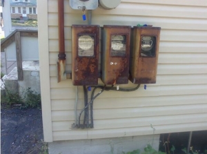 Three, outdated electric boxes are shown outside of a Detroit, MI home before they are replaced.